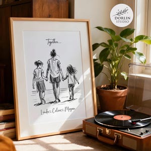 May include: A framed black and white sketch print featuring a mother and two children walking together. The print has the word "Together..." at the top and the names "Linda, Celine, Megan" at the bottom. The frame is light brown.