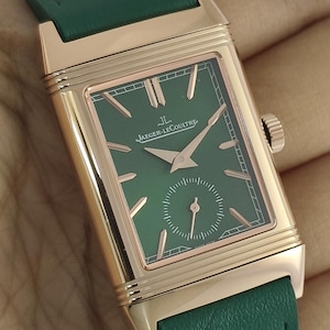Puede incluir: Un reloj de pulsera rectangular con caja de oro rosa y correa de cuero verde. La esfera es verde con manecillas e &iacute;ndices en oro rosa, con el texto Jaeger-LeCoultre y el logotipo JL. En la parte inferior se encuentra una peque&ntilde;a subesfera.
