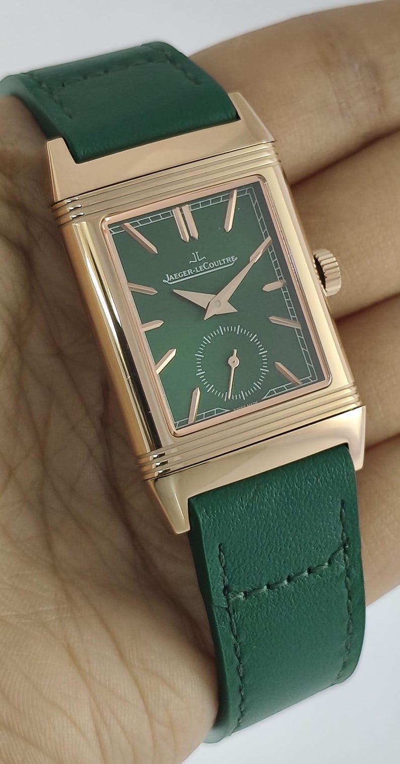 Puede incluir: Un reloj de pulsera rectangular con caja de oro rosa y correa de cuero verde. La esfera es verde con manecillas e &iacute;ndices en oro rosa, con el texto Jaeger-LeCoultre y el logotipo JL. En la parte inferior se encuentra una peque&ntilde;a subesfera.