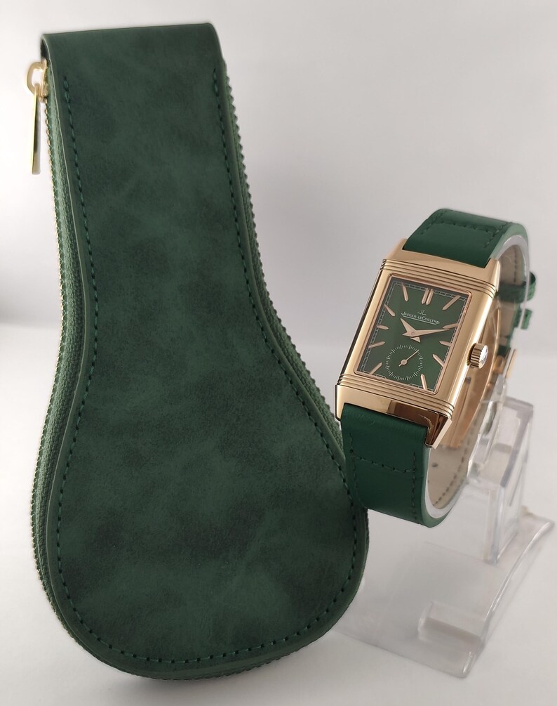 Puede incluir: Un reloj de pulsera rectangular en tono dorado con esfera verde y correa de cuero verde a juego, que presenta un subdial de segundos y marcadores dorados. Junto a &eacute;l, un estuche de almacenamiento verde oscuro en forma de gota con cremallera.