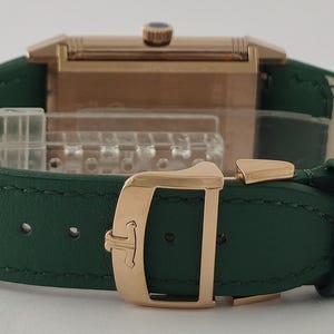 Puede incluir: Un reloj rectangular con caja de oro rosa y correa de cuero verde oscuro. El reloj cuenta con un cierre desplegable de oro rosa con un logotipo grabado y una peque&ntilde;a corona con un detalle azul en el borde superior de la caja rectangular.
