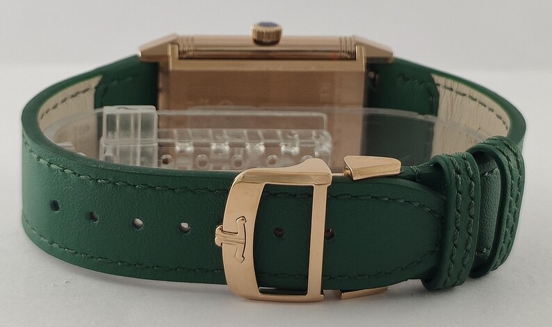 Puede incluir: Un reloj rectangular con caja de oro rosa y correa de cuero verde oscuro. El reloj cuenta con un cierre desplegable de oro rosa con un logotipo grabado y una peque&ntilde;a corona con un detalle azul en el borde superior de la caja rectangular.