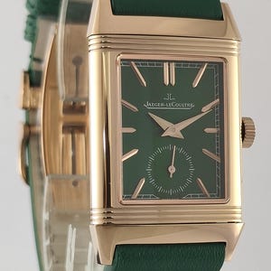 Puede incluir: Un reloj de pulsera rectangular con caja de oro rosa y esfera verde oscuro. La esfera presenta marcadores de hora en oro rosa, manecillas a juego y un peque&ntilde;o subdial de segundos en la parte inferior. El texto Jaeger-LeCoultre est&aacute; impreso en blanco. Correa de cuero verde.