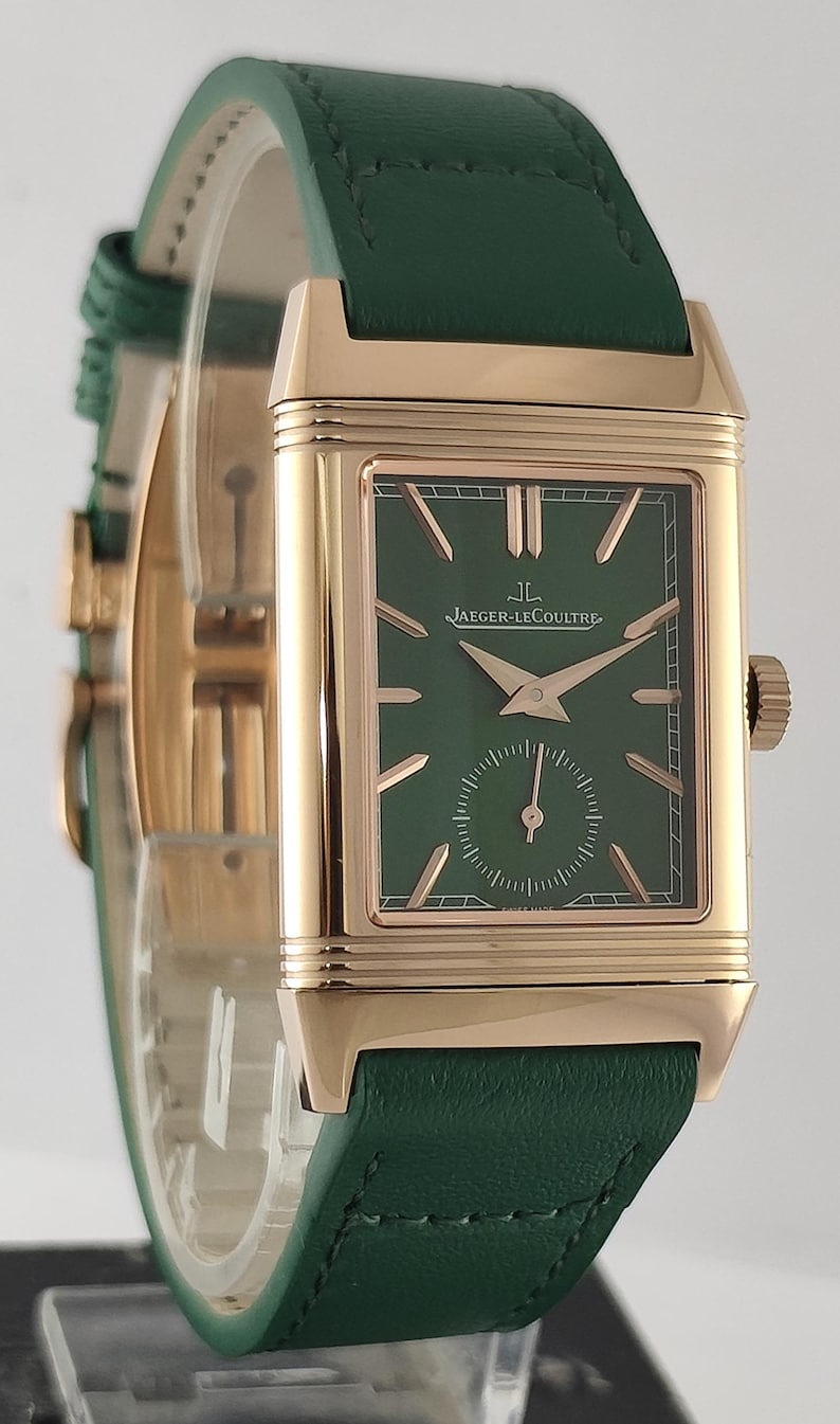 Puede incluir: Un reloj de pulsera rectangular con caja de oro rosa y esfera verde oscuro. La esfera presenta marcadores de hora en oro rosa, manecillas a juego y un peque&ntilde;o subdial de segundos en la parte inferior. El texto Jaeger-LeCoultre est&aacute; impreso en blanco. Correa de cuero verde.