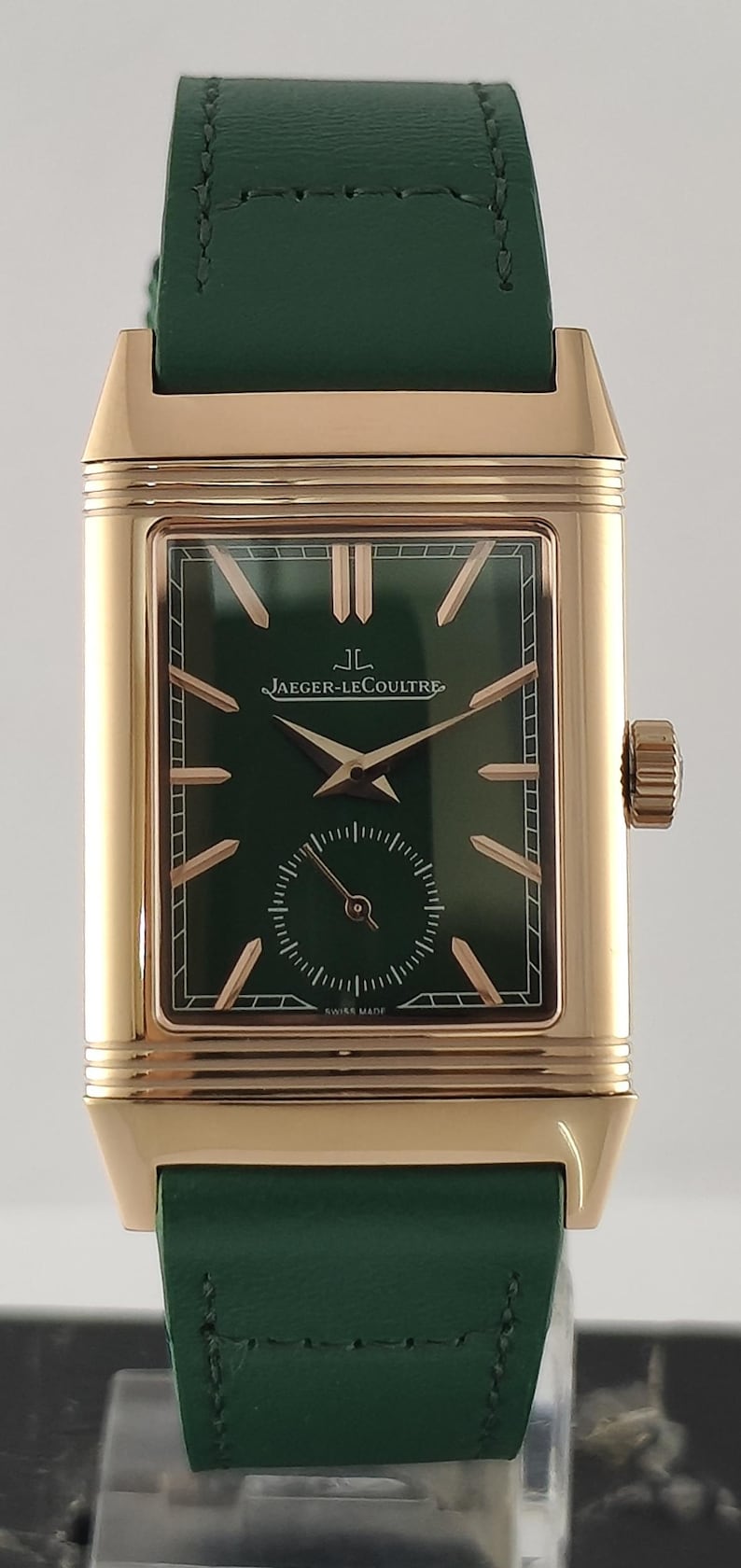 Puede incluir: Un reloj de pulsera rectangular con caja de oro rosa y esfera verde oscuro. La esfera presenta marcadores de hora dorados, manecillas doradas y una subesfera de segundos en la parte inferior. El texto Jaeger-LeCoultre est&aacute; impreso en blanco. Correa de cuero verde.