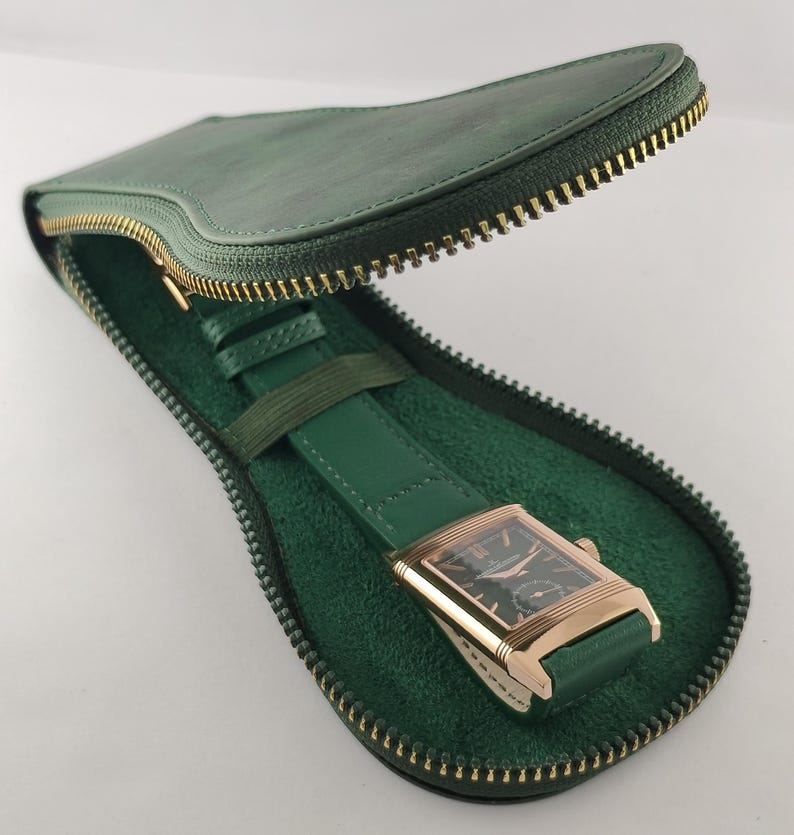 Puede incluir: Un reloj de pulsera rectangular con caja dorada y esfera negra, con correa de cuero verde, guardado en un estuche de viaje de cuero verde en forma de l&aacute;grima con cremallera de metal dorado y forro interior de color verde suave.