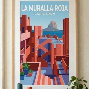 Può includere: Stampa artistica incorniciata di La Muralla Roja a Calpe, Spagna. La stampa presenta un design architettonico geometrico nei toni del rosso, rosa e blu, con il testo "LA MURALLA ROJA" e "CALPE, SPAIN". La stampa è esposta sopra un mobile in legno con vasi e libri.