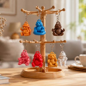 Könnte beinhalten: Ein drehbarer Präsentationsständer aus Holz mit sieben bunten froschförmigen Schlüsselanhängern. Die Anhänger zeigen Frösche in verschiedenen Posen und Farben, darunter Orange, Blau, Braun, Pink, Rot, Gelb und Weiß, jeweils an einem silbernen Metallring.