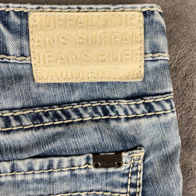 May include: A white ceramic mug with a black handle and the text "But First, Coffee" in a bold, black font. The mug is set against a blurred background, suggesting a cozy setting. The mug appears to be approximately 4 inches tall.