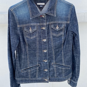 May include: A dark blue denim jacket with a button closure and multiple pockets. The jacket has a Tommy Hilfiger logo label on the left side of the chest.