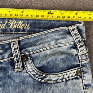 May include: Close-up of blue denim jeans with white stitching and a pocket. The jeans have the brand name "void Bitton" embroidered on them. A yellow measuring tape is placed across the top of the jeans, showing measurements from 20 to 39 inches.