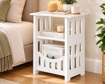 May include: A white wooden side table with a rectangular top, an open middle shelf, and a lower storage compartment with a curved front panel. The table features vertical slat side detailing and holds books titled The Kinfolk and Cereal.