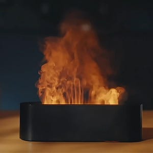Peut inclure: Une cheminée de table noire et rectangulaire avec un effet de flamme réaliste. Les flammes sont orange et jaune, créant une ambiance chaleureuse. Un petit pot carré blanc avec une plante est visible en arrière-plan.
