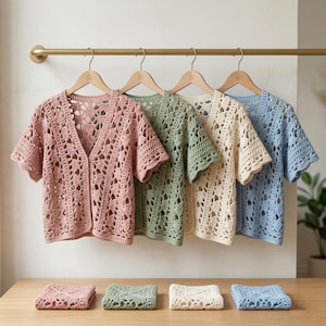 May include: Four pastel-coloured, open-front crochet cardigans: pink, green, cream, and blue. Each hangs on a wooden hanger. Matching folded squares of crochet fabric sit below, displaying the openwork design of the garments.