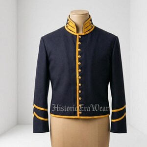 Peut inclure: Une veste de style militaire bleu marine foncé avec un col montant, des manches longues et une fermeture boutonnée sur le devant. Le vêtement est orné d'un passepoil jaune vif le long du col, de la patte de boutonnage et des poignets.