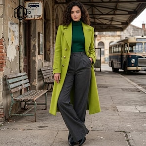May include: A long lime green wool coat with gold buttons worn over a dark green ribbed turtleneck sweater and charcoal grey high-waisted trousers. The coat features a notched lapel and long sleeves, while the trousers have a straight-leg cut.