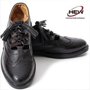 Könnte beinhalten: Ein Paar schwarze Lederschuhe im Brogue-Stil mit dekorativen Perforationen, schwarzen Schnürsenkeln und schwarzen Quasten an der Schnürung. Das Innere ist hellbraun und mit der Größe 41 gekennzeichnet. Das Logo HEW HistoricEraWear ist sichtbar.
