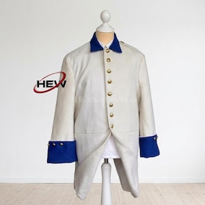May include: A cream-colored historical coat with a blue collar and cuffs. The coat features gold buttons down the front and is displayed on a mannequin. The cuffs have three gold buttons. The logo "HEW" is visible on the left side.