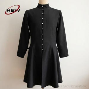 May include: A black long-sleeved coat featuring a high mandarin collar and a front button closure with small silver-toned buttons. The garment has a fitted bodice that flares slightly at the waist, extending to a knee-length hemline.