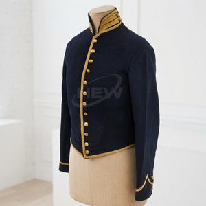 May include: A dark navy blue military-style jacket featuring a high collar with gold trim, a front button closure with gold-toned buttons, and gold piping along the edges. The cuffs are detailed with gold trim in a decorative wave pattern.