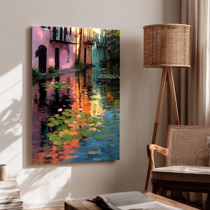 May include: A vertical canvas print of a canal scene with buildings in shades of pink, orange, and blue. The water reflects the colors of the buildings and the sky, with lily pads and pink flowers floating on the surface.