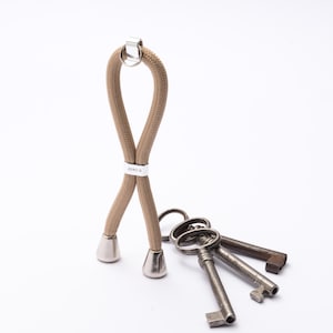 May include: A tan rope keychain with silver details, holding several antique metal keys. The keychain has the text "ZERO G" on a silver band. The keys are various sizes and show signs of age.
