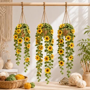 May include: Three hanging crochet baskets filled with green foliage and yellow sunflowers. The baskets are suspended from a wooden rod by brown rope. The sunflowers cascade down, creating a decorative and natural aesthetic.