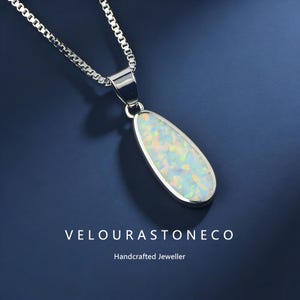May include: A silver necklace featuring a teardrop opal pendant. The opal displays a white base with iridescent colours. The pendant is set in a silver bezel and suspended from a fine chain. The text "VELOURASTONECO" and "Handcrafted Jeweller" are at the bottom.