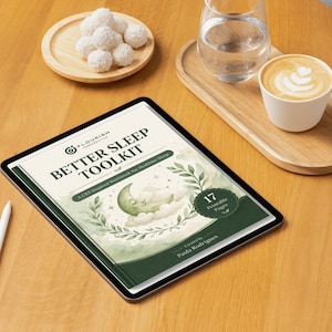 Puede incluir: Una tableta digital muestra el "Better Sleep Toolkit" con un diseño de luna y nube. Un lápiz óptico blanco, un café con leche, un vaso de agua y un plato con dulces blancos están sobre una mesa de madera. La tableta tiene 17 páginas imprimibles.