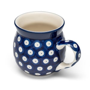 Könnte beinhalten: Eine Keramik-Tasse mit dunkelblauem Äußeren, verziert mit einem Muster aus weißen Punkten. Der Innenraum ist cremefarben, und der Griff ist weiß mit blauen Punkten. Die Tasse hat eine abgerundete Form.