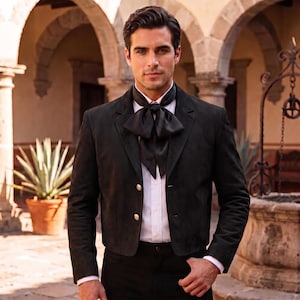 May include: A black suede blazer with two silver buttons, worn over a crisp white button-down shirt. A black satin cravat is tied neatly at the neck. The blazer features a structured collar, long sleeves, and a tailored fit, creating a formal look.