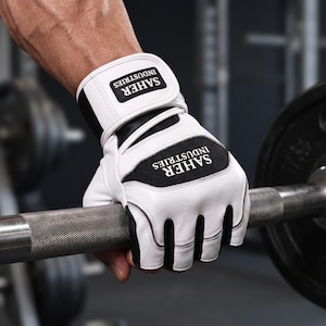 May include: A white and black fingerless weightlifting glove with a wrist strap featuring the text SAHER INDUSTRIES. The glove has a white leather-like exterior with black mesh panels and a black and white logo patch on the wrist and back of hand.