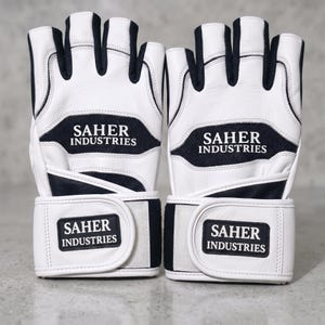 May include: A pair of fingerless gloves in white and black with a textured finish. The gloves feature the text SAHER INDUSTRIES printed on the back of the hand and on the adjustable wrist strap. The design includes black mesh panels between the fingers.