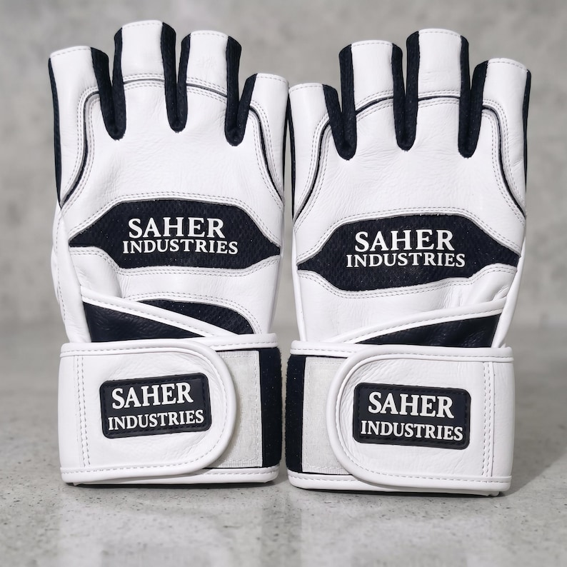 May include: A pair of fingerless gloves in white and black with a textured finish. The gloves feature the text SAHER INDUSTRIES printed on the back of the hand and on the adjustable wrist strap. The design includes black mesh panels between the fingers.