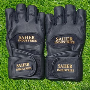 May include: A pair of black fingerless gloves featuring textured leather panels and mesh inserts. The text SAHER INDUSTRIES is printed in gold on the back of the hand and on the adjustable hook-and-loop wrist strap of each glove.