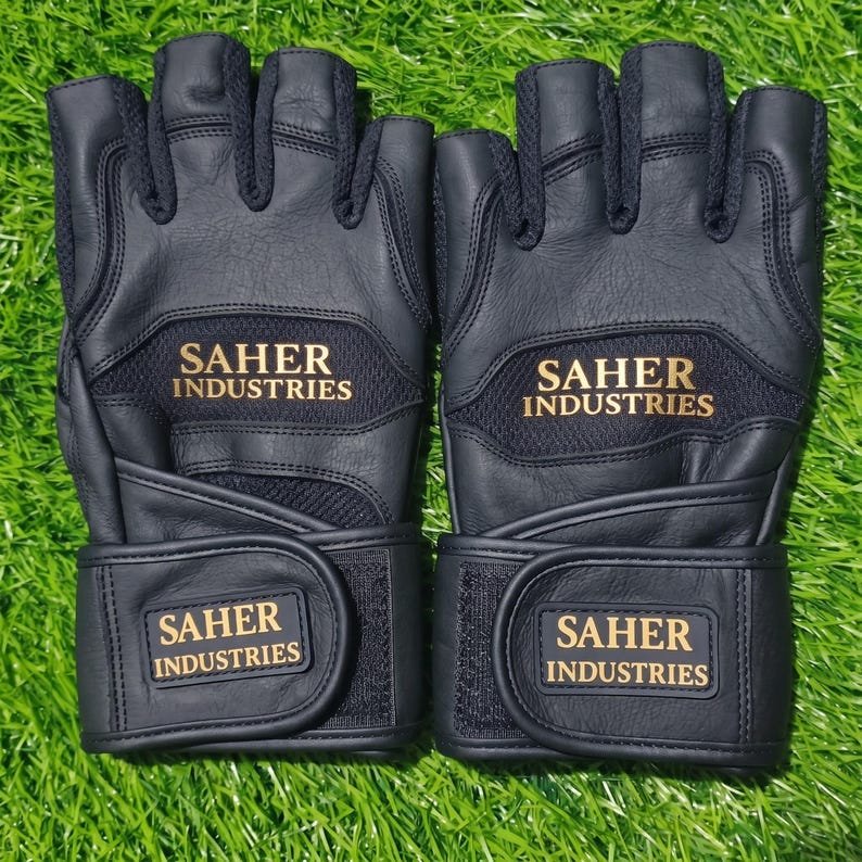 May include: A pair of black fingerless gloves featuring textured leather panels and mesh inserts. The text SAHER INDUSTRIES is printed in gold on the back of the hand and on the adjustable hook-and-loop wrist strap of each glove.