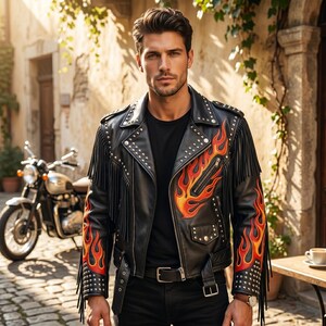 Puede incluir: Una chaqueta de moto de cuero negro con tachuelas metálicas plateadas, largos flecos en las mangas y un diseño gráfico de llamas en naranja y rojo vibrante en el pecho y los antebrazos, sobre una camiseta negra lisa y pantalones negros.
