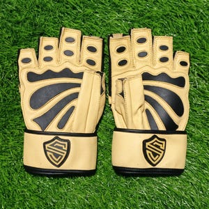 May include: A pair of fingerless gloves in beige and black. The gloves feature black rubberized padding on the fingers and palm area, with a beige wrist strap displaying a black shield-shaped logo with a stylized letter S in the center.