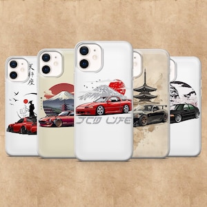 May include: A collection of white phone cases featuring Japanese-inspired designs. Each case showcases a different car illustration with elements like Mount Fuji, a rising sun, and Japanese text. The phrase "JDM LIFE" is printed on one case.