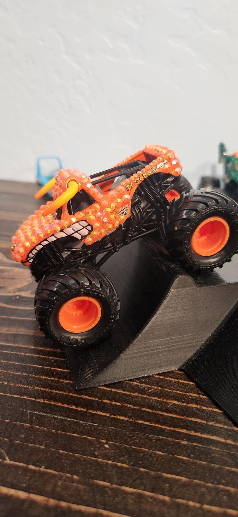 May include: Orange monster truck toy with black wheels and orange accents. The truck has a bull-like design with the words "El Toro Loco" on the side. The wheels are large and the truck is on a ramp.