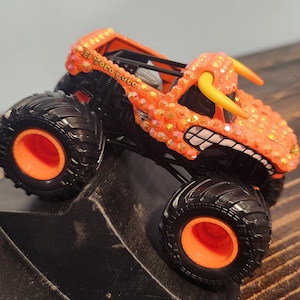 May include: Orange and black toy monster truck with the text "El Toro Loco". The truck has large black tires with orange rims, and a detailed orange body with yellow horns and a toothy grin.