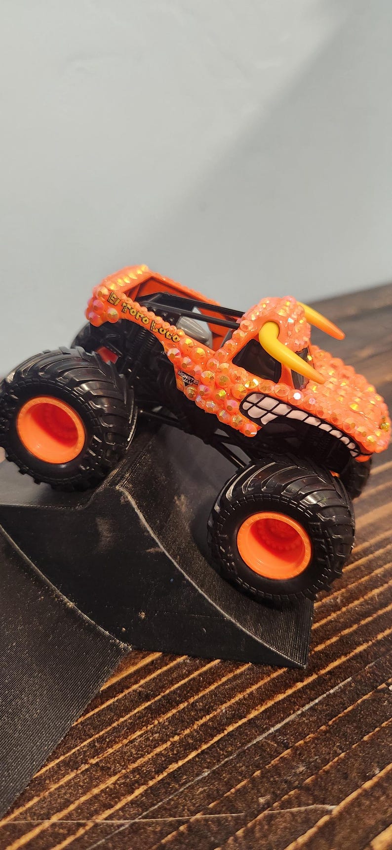 May include: Orange and black toy monster truck with the text "El Toro Loco". The truck has large black tires with orange rims, and a detailed orange body with yellow horns and a toothy grin.