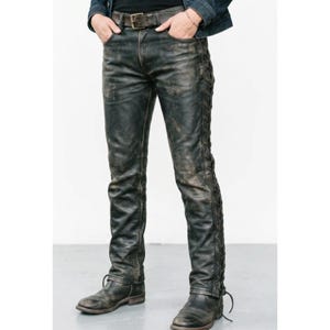May include: Distressed black leather pants featuring a lace-up detail running down the outer side of each leg. The pants have a standard waistband with belt loops, a front button closure, and a weathered finish throughout the dark material.
