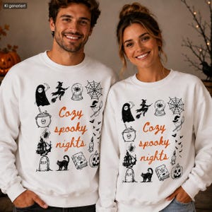 Könnte beinhalten: Zwei weiße Sweatshirts mit Rundhalsausschnitt und dem orangefarbenen Schriftzug Cozy spooky nights, umgeben von schwarzen Illustrationen eines Geistes, einer Hexe, einer Kristallkugel, eines Spinnennetzes, eines Kessels, einer Spinne, eines Spukhauses, eines Grabsteins, einer Katze, eines Buches, einer Kerze und eines Kürbisses.
