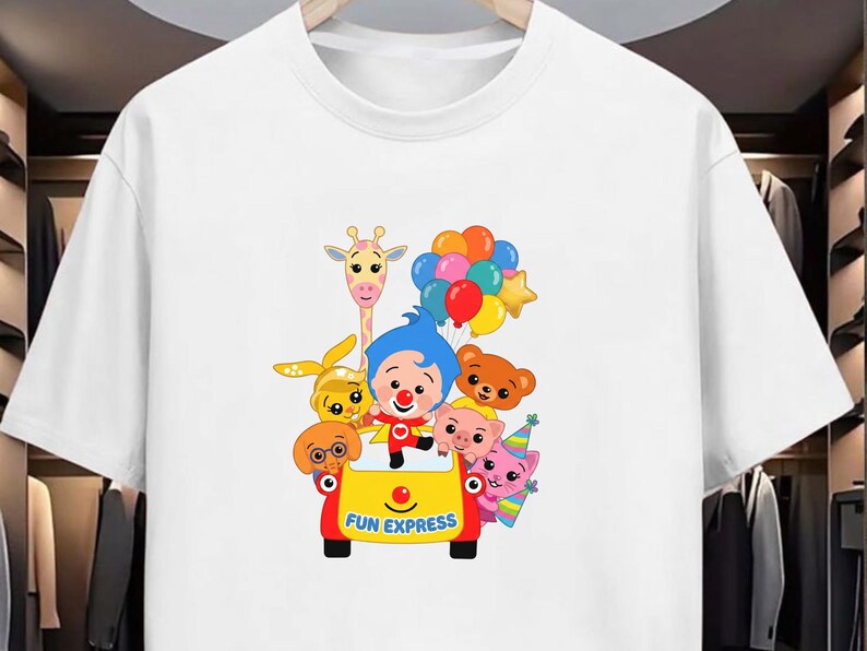 Puede incluir: Camiseta blanca con un dise&ntilde;o de dibujos animados colorido. El gr&aacute;fico muestra un payaso y varios animales de dibujos animados en un veh&iacute;culo amarillo con la inscripci&oacute;n "FUN EXPRESS". El dise&ntilde;o tambi&eacute;n incluye globos y una jirafa.