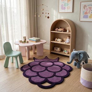 May include: A purple rug shaped like a cluster of grapes with a scalloped edge, placed on a wooden floor. The rug features a dark purple outline and a lighter purple interior, creating a textured, layered appearance in a room with children's furniture.