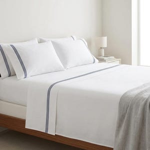 Puede incluir: Juego de ropa de cama blanca con rayas azul marino. El juego incluye una sábana bajera, una sábana encimera y fundas de almohada. La cama tiene un marco de madera y una manta gris está sobre los pies de la cama.