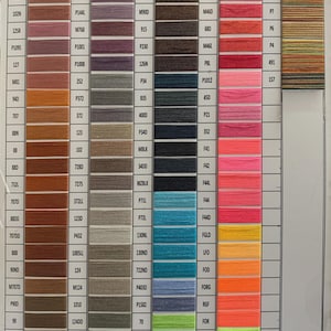 May include: A color chart displaying a wide array of thread colors, organized in vertical columns. Each thread color is labeled with a unique code, ranging from warm browns to vibrant pinks and greens, ideal for crafting.