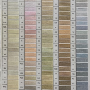 May include: A color chart displaying a wide array of thread colors, ranging from white and beige to various shades of green, brown, and blue. Each color is labeled with a unique code, providing a comprehensive selection for crafting and sewing projects.