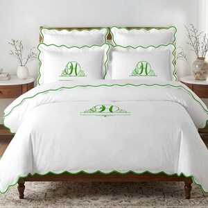 May include: A white bedding set featuring a scalloped green trim and a green embroidered letter H monogram centered on the duvet cover and two pillowcases. The set includes two additional plain white pillowcases with matching green scalloped edges.